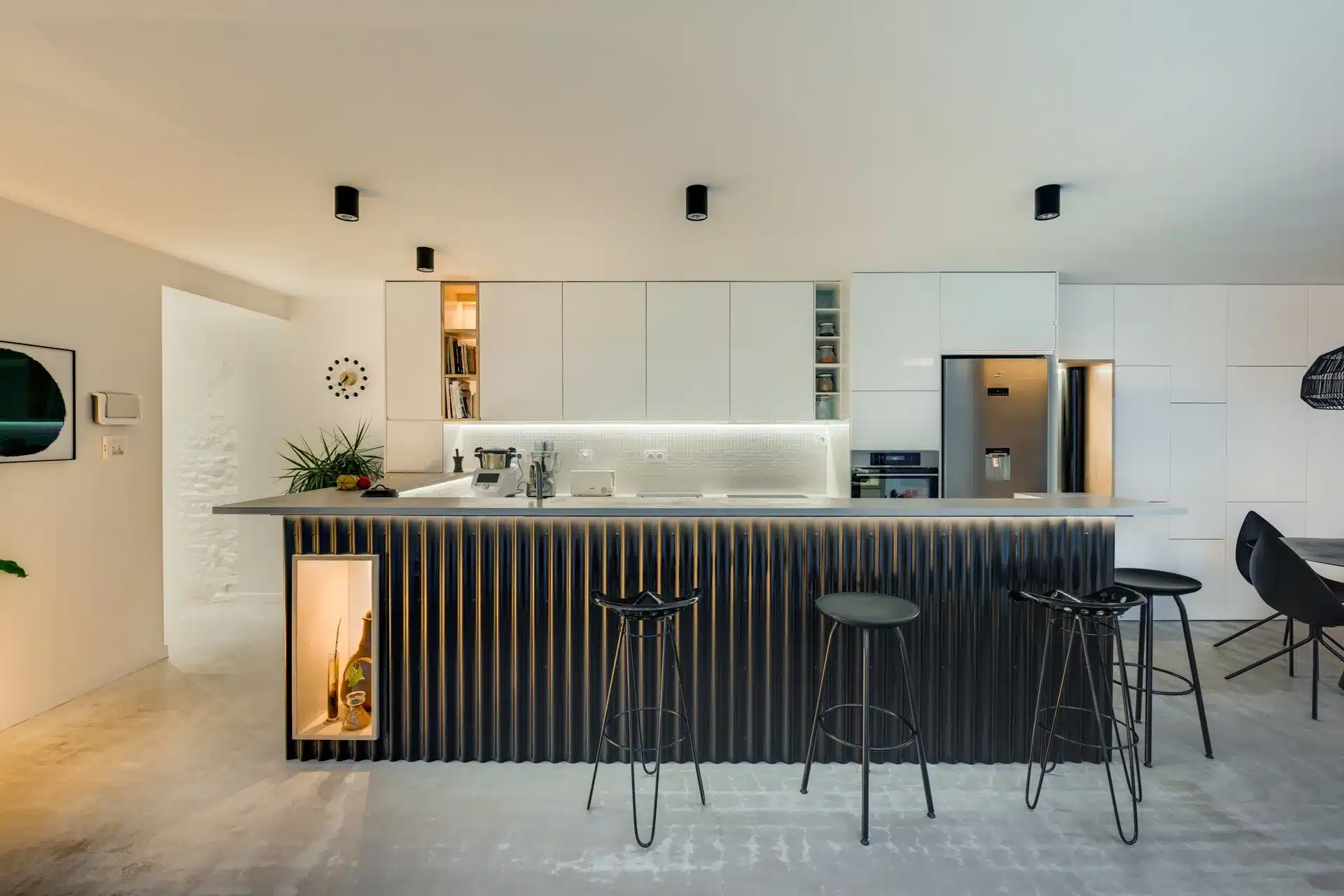 Cuisine contemporaine blanche et noire avec îlot central à lamelles, électroménagers inox, tabourets hauts et rangements épurés