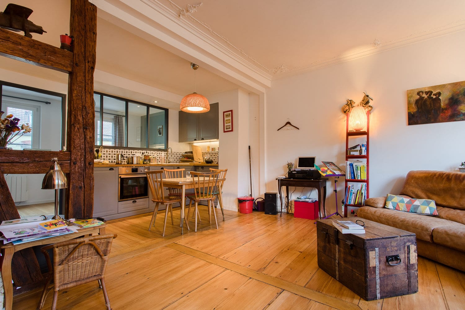 Loft spacieux aux murs blancs, poutre apparente en bois, cuisine ouverte avec carrelage géométrique, canapé marron et parquet clair