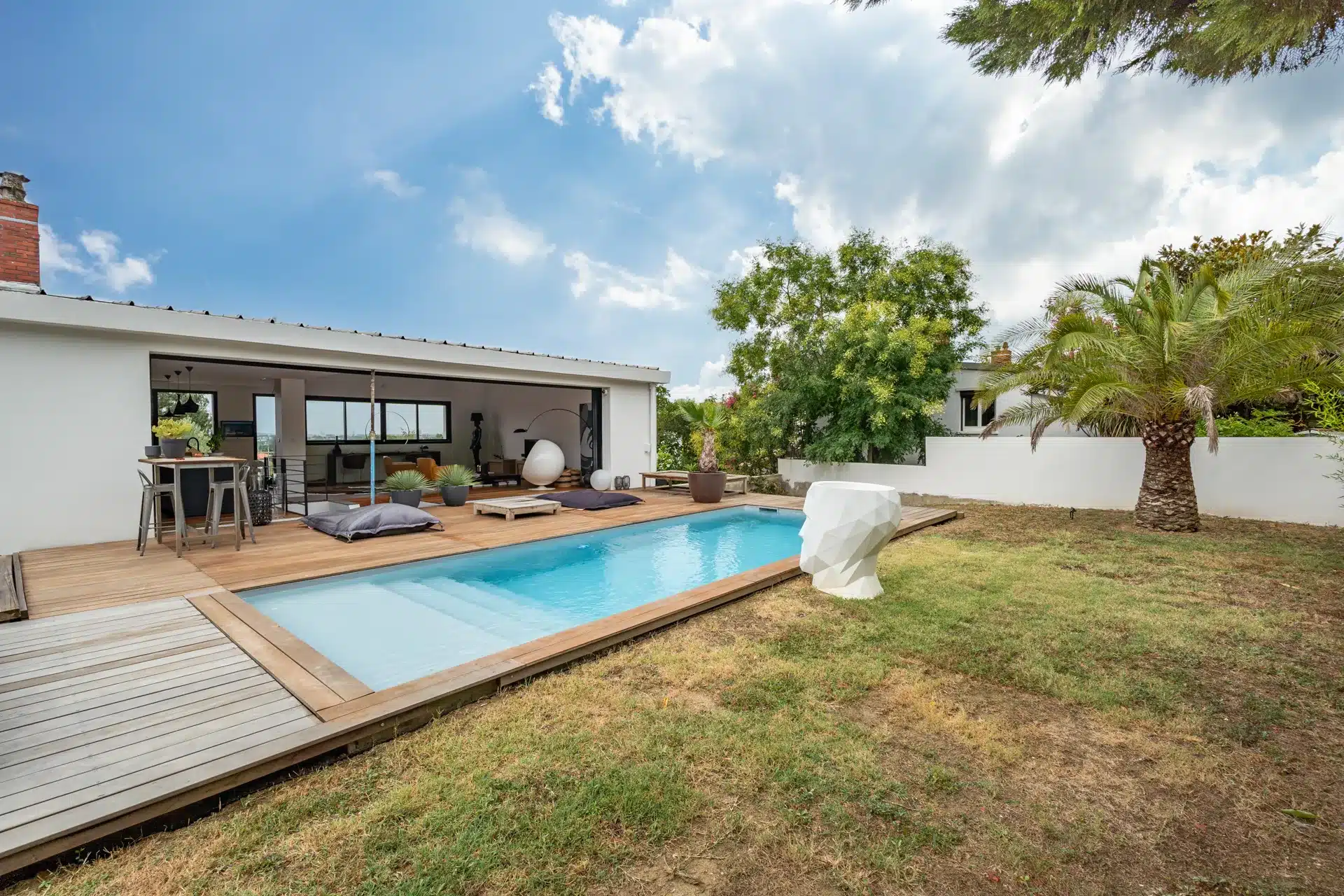 Maison contemporaine blanche avec piscine bleue, terrasse en bois et palmier, sous ciel dégagé