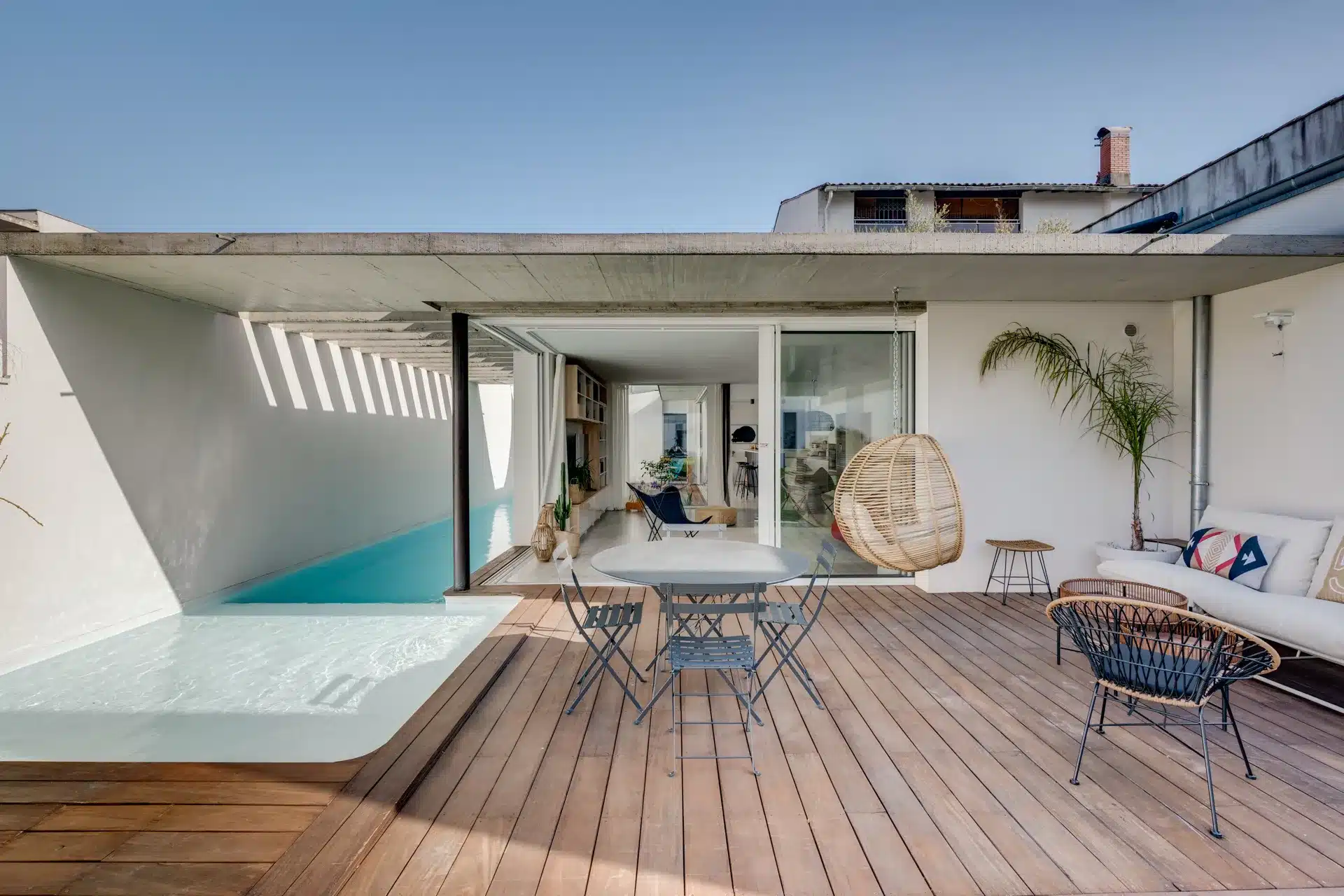 Terrasse spacieuse avec piscine turquoise, mobilier design et baies vitrées ouvertes sur salon lumineux