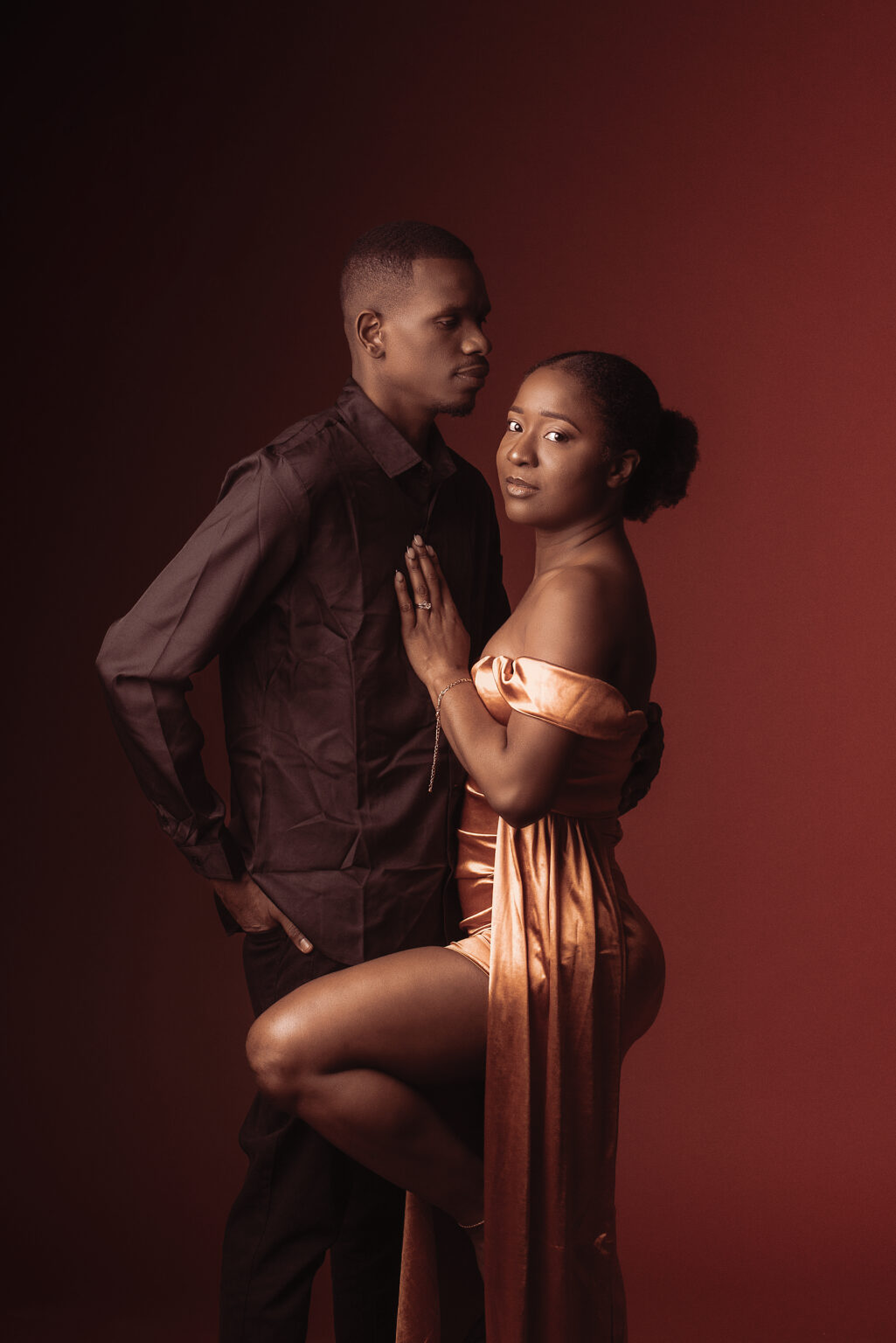 Couple posant ensemble sur fond rouge, femme en robe or et homme en chemise noire