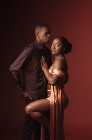 Couple posant ensemble sur fond rouge, femme en robe or et homme en chemise noire