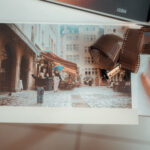 Main posant sur une pellicule photo argentique Kodak, bobine marron à côté, imprimé vintage d'une rue ancienne en arrière-plan