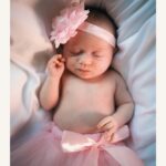 Bébé en robe rose avec une fleur dans les cheveux, paisiblement allongé sur un fond doux.