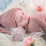 Photo d'un nouveau-né endormi, entouré de fleurs délicates, capturé dans un style doux et naturel.