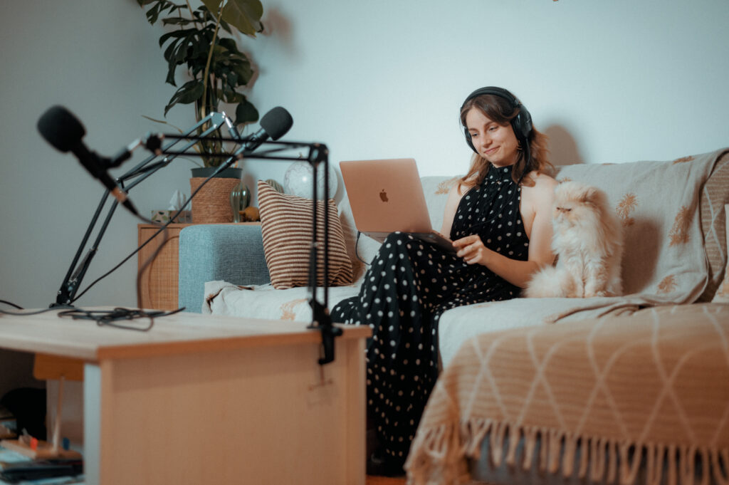 Femme assise sur un canapé, casque audio sur les oreilles, ordinateur portable à la main, micro professionnel en face d'elle
