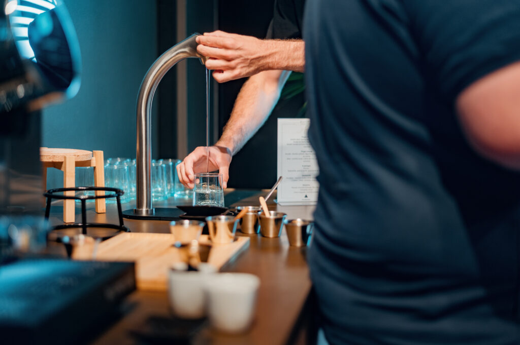 Formateur verse de l'eau chaude dans un verre lors d'un atelier de preparation du cafe, materiel de barista sur la table