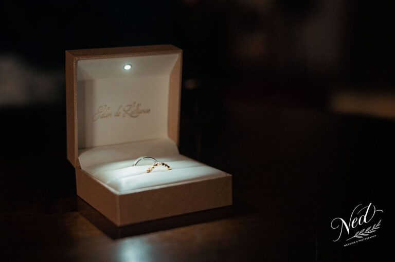 Deux alliances en or blanc et or rose posées dans un écrin marron ouvert, petit projecteur intérieur illuminant les bagues
