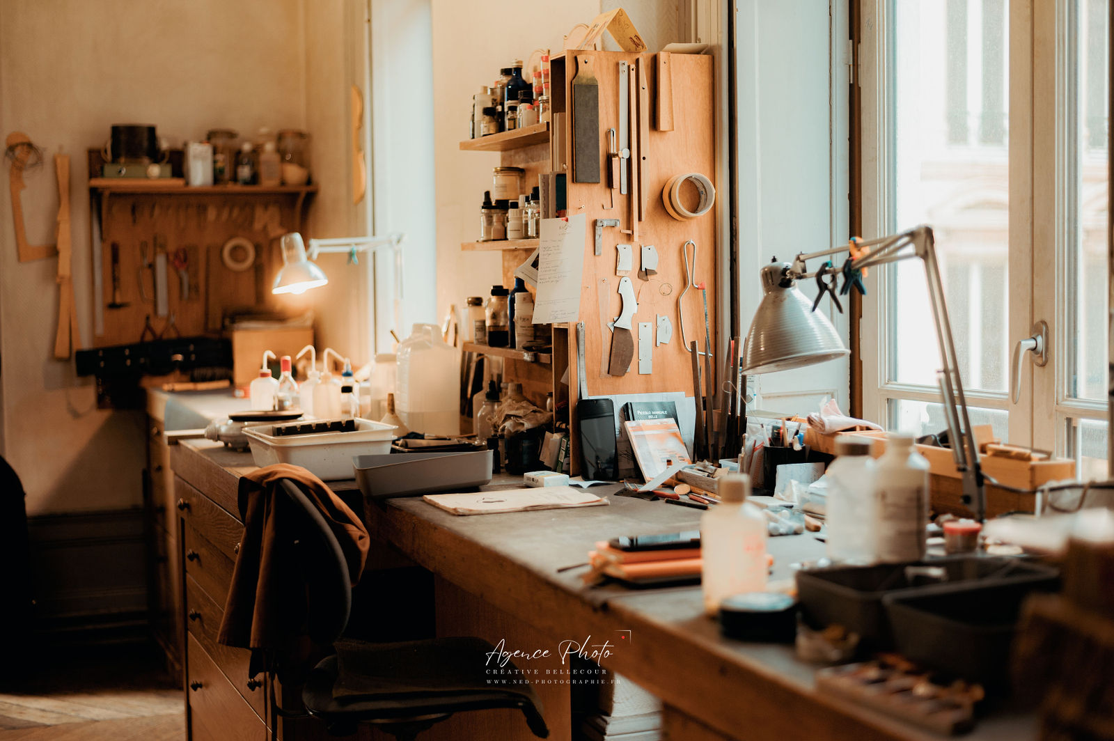 Atelier de photographe avec etabli en bois, outils de retouche, panneaux perforés d'organisation et fenêtres claires