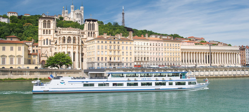 Bateau blanc de croisière navigue sur le Rhône devant la Basilique Notre-Dame de Fourvière et l'architecture historique de Lyon