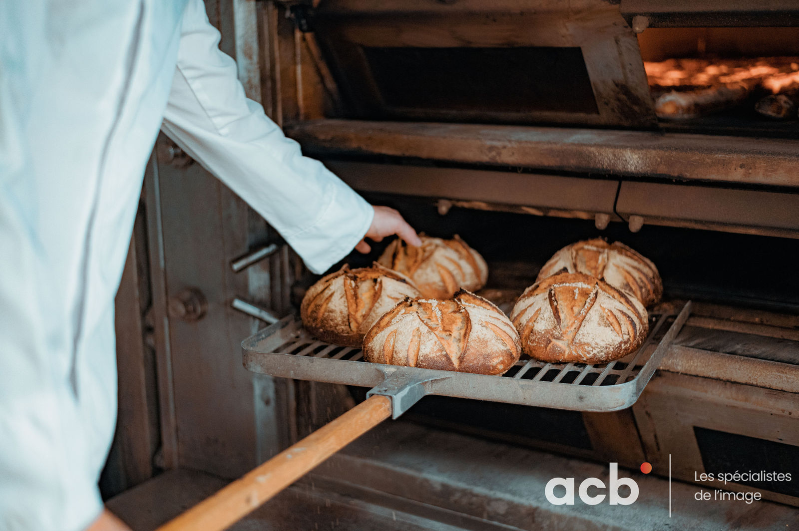 Boulanger en veste blanche sort des pains artisanaux dorés du four avec une pelle en bois