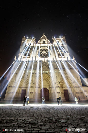 Façade de la Cathédrale Saint-Jean éclairée de nuit avec projecteurs, quelques personnes debout sur le parvis en pavés