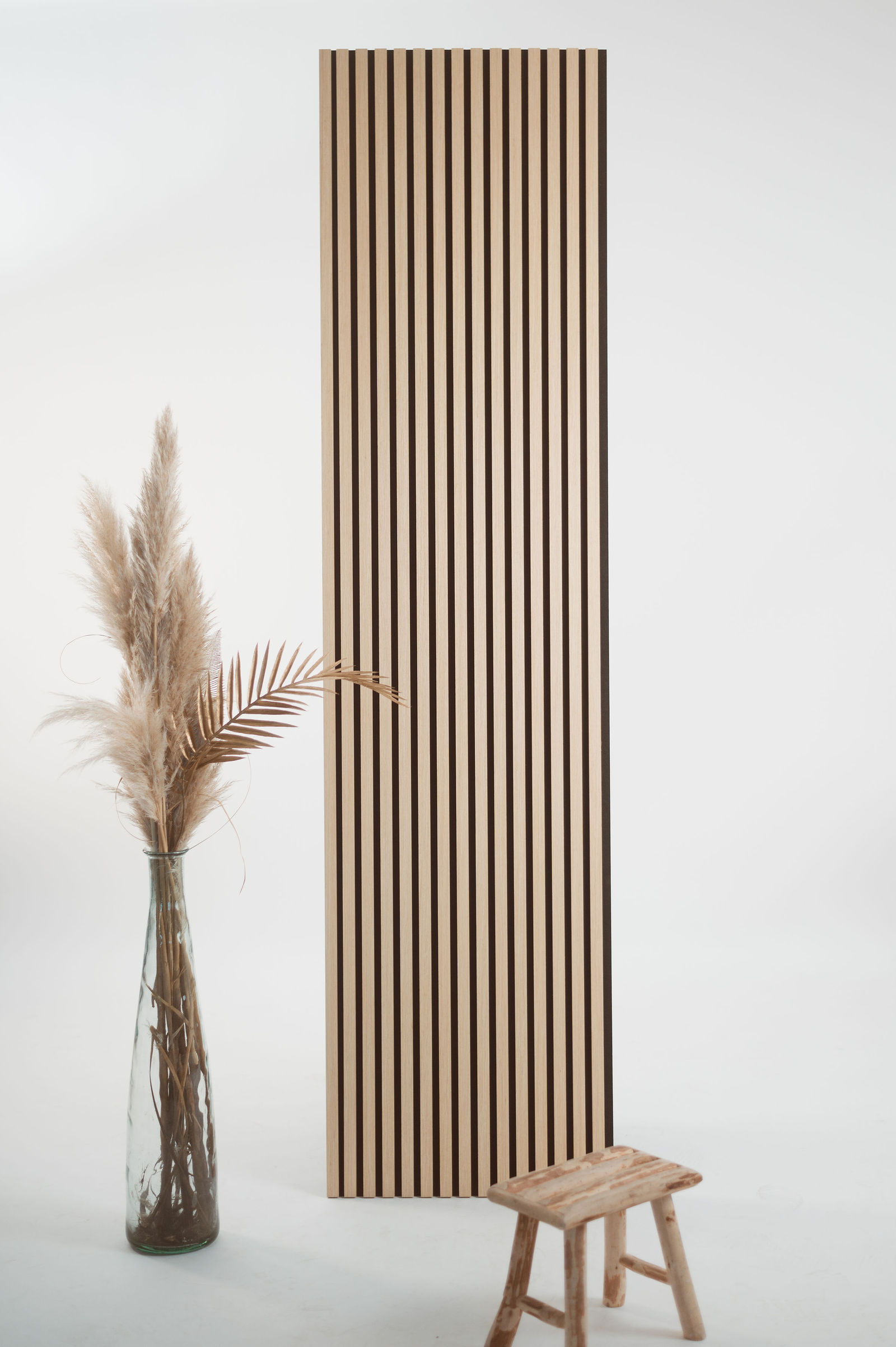 Panneau en bois à lames verticales face à un tabouret rustique et vase avec fleurs séchées, décor épuré