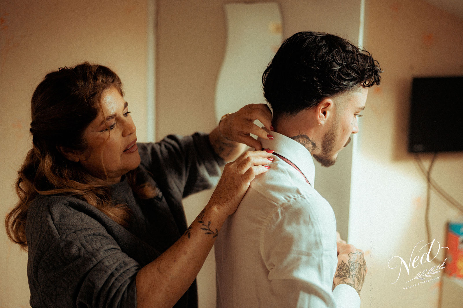 Femme aux cheveux roux enlacant un homme de profil dans un intérieur aux murs beige, lumière chaude