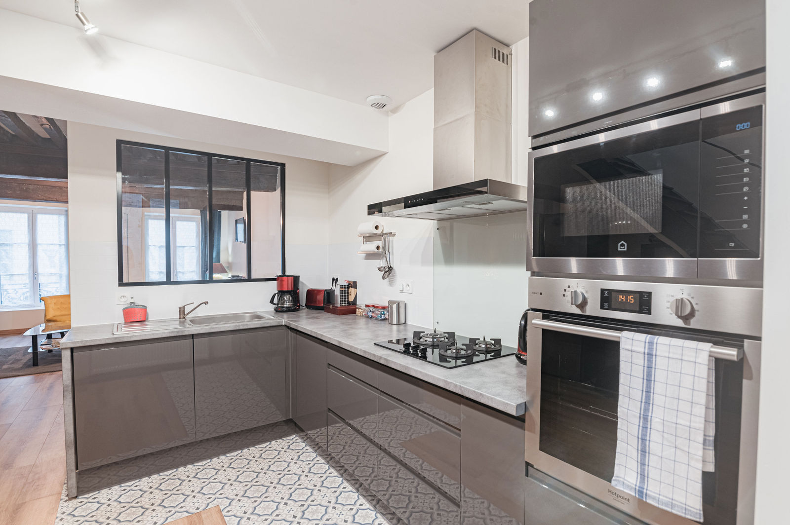 Cuisine contemporaine avec mobilier gris, plan de travail marbre, électroménager inox et fenêtre noire donnant sur séjour lumineux