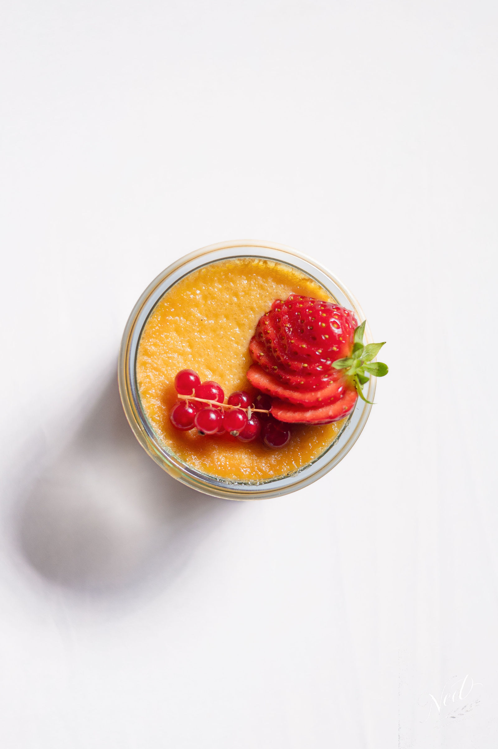 Verre de mousse abricot garni de fraise et groseilles sur fond blanc, vue de dessus