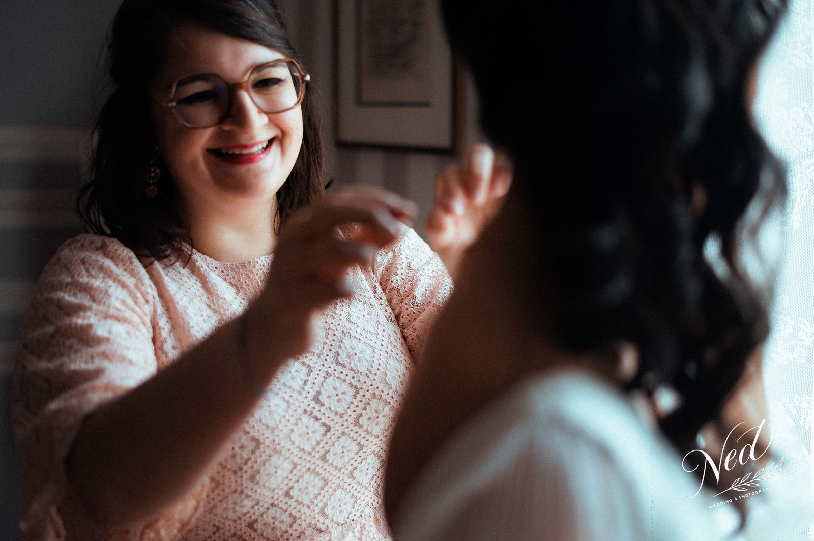 Femme aux lunettes en pull rose sourit en regardant sa copine, lumière naturelle du jour