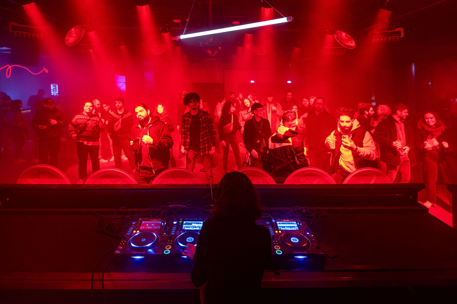 DJ vu de dos à la console devant une piste de danse rouge avec une cinquantaine de personnes en mouvement