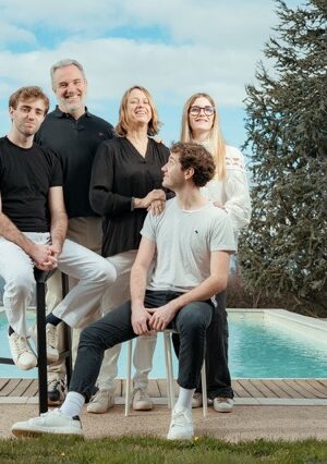 Cinq personnes souriantes posent ensemble devant une piscine turquoise et des arbres, en extérieur par beau temps