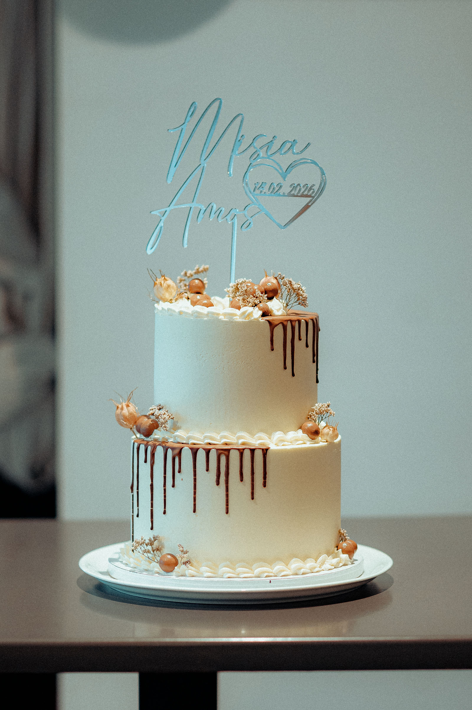 Gâteau de mariage deux étages en crème blanche, décoration de boules dorées et fleurs séchées, pique coeur avec noms et date