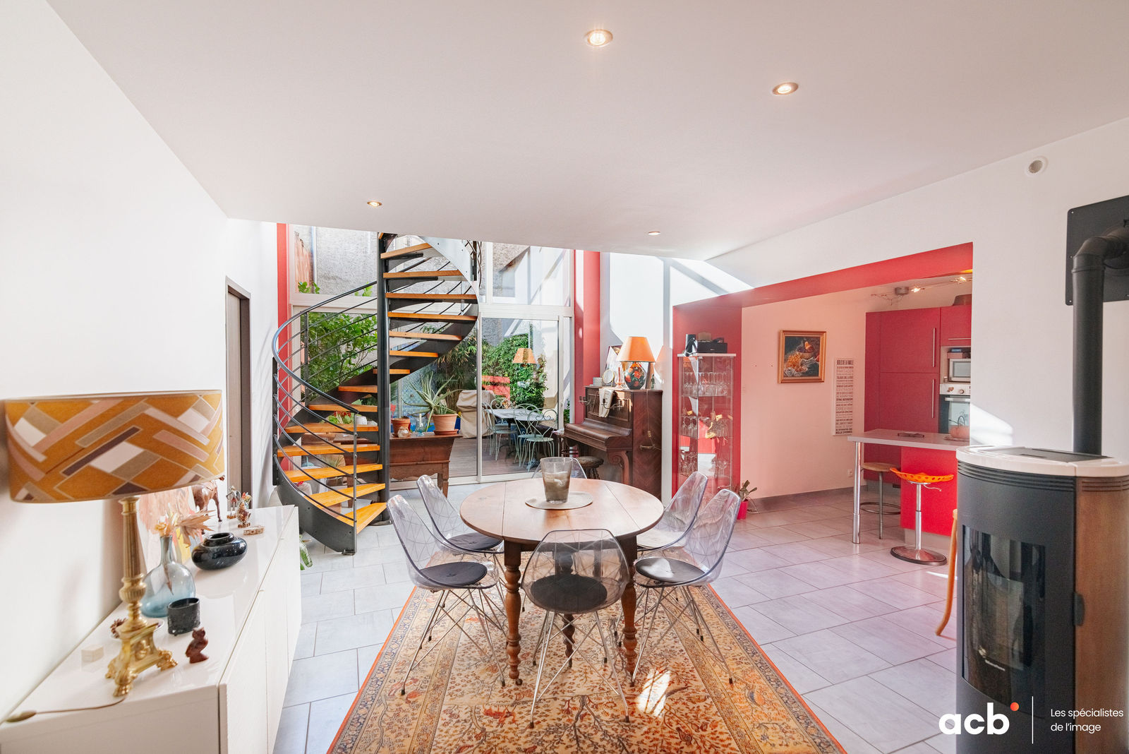 Intérieur design avec escalier en colimaçon noir et bois, salle à manger avec table ronde, murs rouges et blancs, baies vitrées.