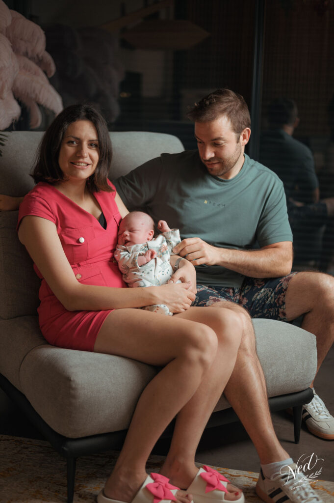 Jeune couple assis sur un canapé gris tenant leur bébé nouveau-né dans un intérieur moderne