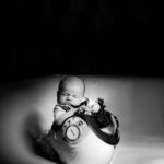 Bébé de quelques semaines assis dans un droid blanc et noir, tenant un petit jouet chat noir