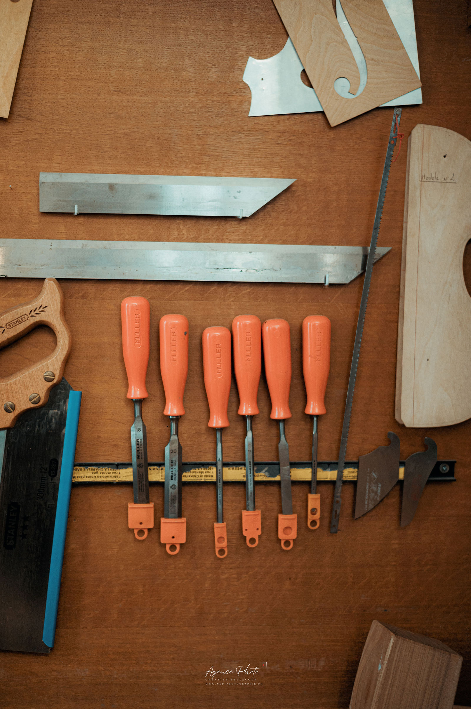Six ciseaux orange alignés sur un établi en bois avec outils de lutherie et pièces de bois