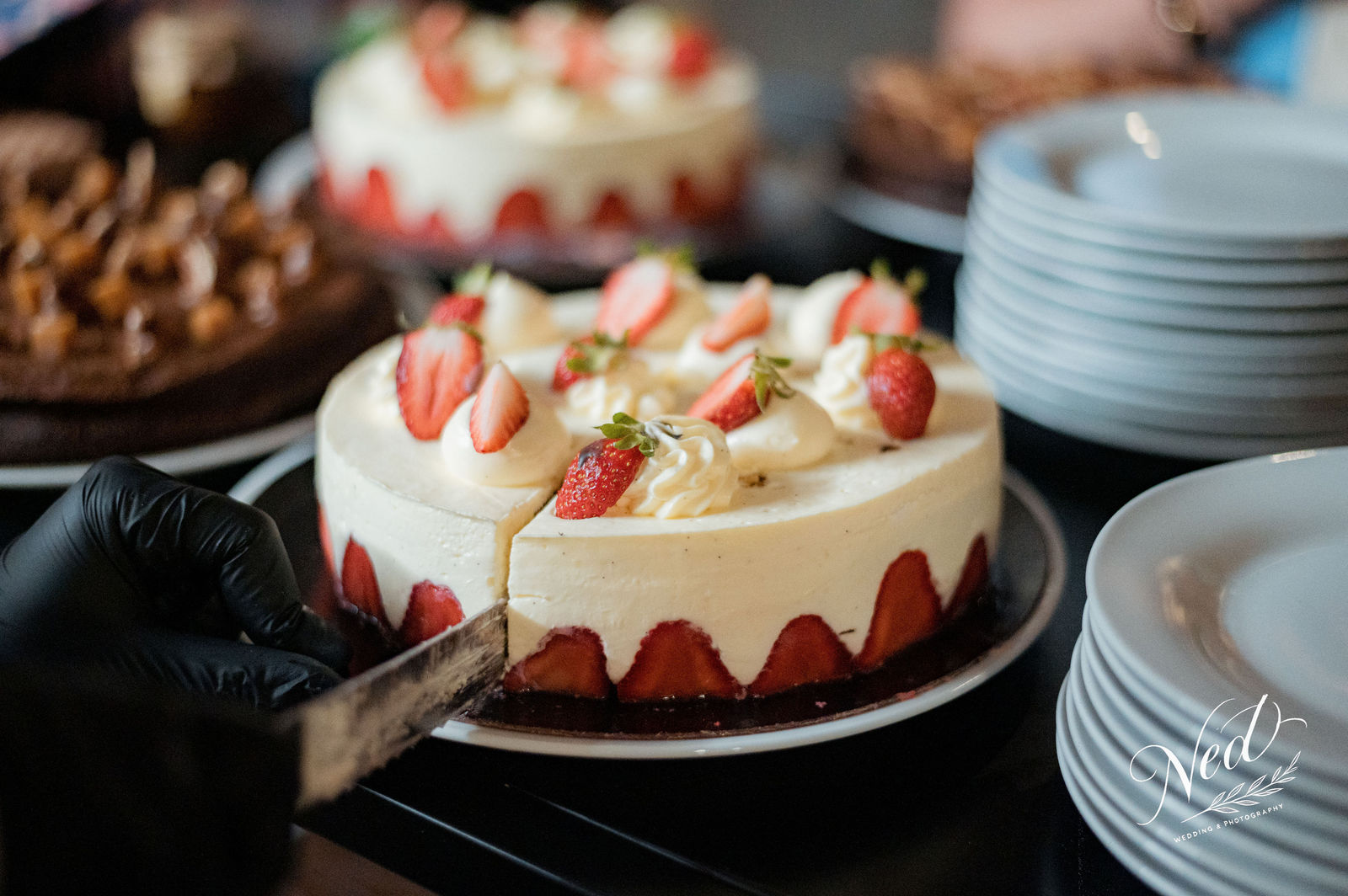 Gâteau aux fraises fraîches avec glaçage blanc et crème pâtissière, entouré d'assiettes et d'autres pâtisseries