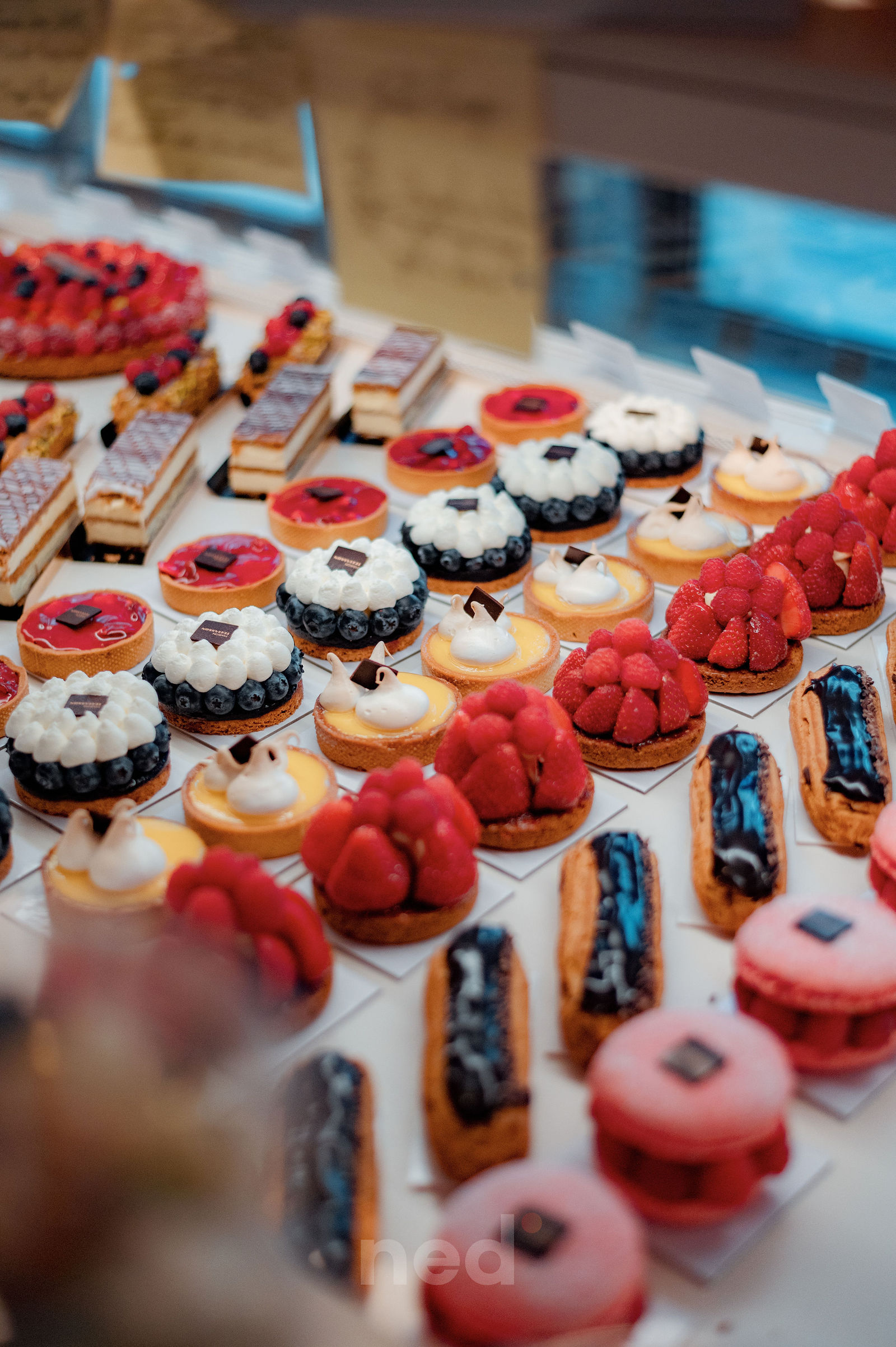 Assortiment de petits gâteaux et tartelettes alignés sur table, décorés de framboises, myrtilles et glaçage rose et noir