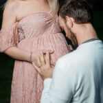 Futur père embrassant le ventre de sa compagne enceinte vêtue d'une robe rose, fond noir