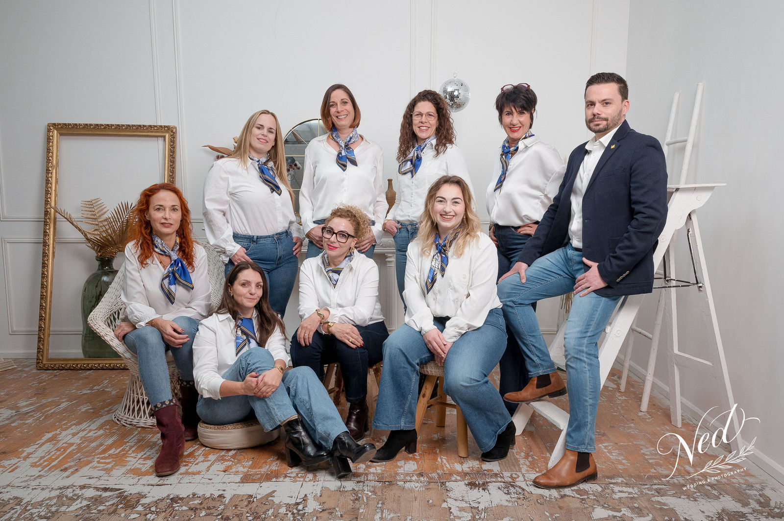 Groupe de dix personnes en chemises blanches et foulards bleus posent ensemble dans un studio épuré, assis et debout devant un mur blanc.