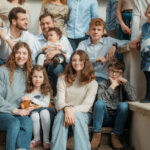 Grande famille de trois générations posée sur des marches en pierre, parents et enfants souriants en vêtements pastel et bleu