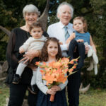 Grands-parents avec trois enfants posent devant un grand arbre, la fillette tient un bouquet de fleurs oranges
