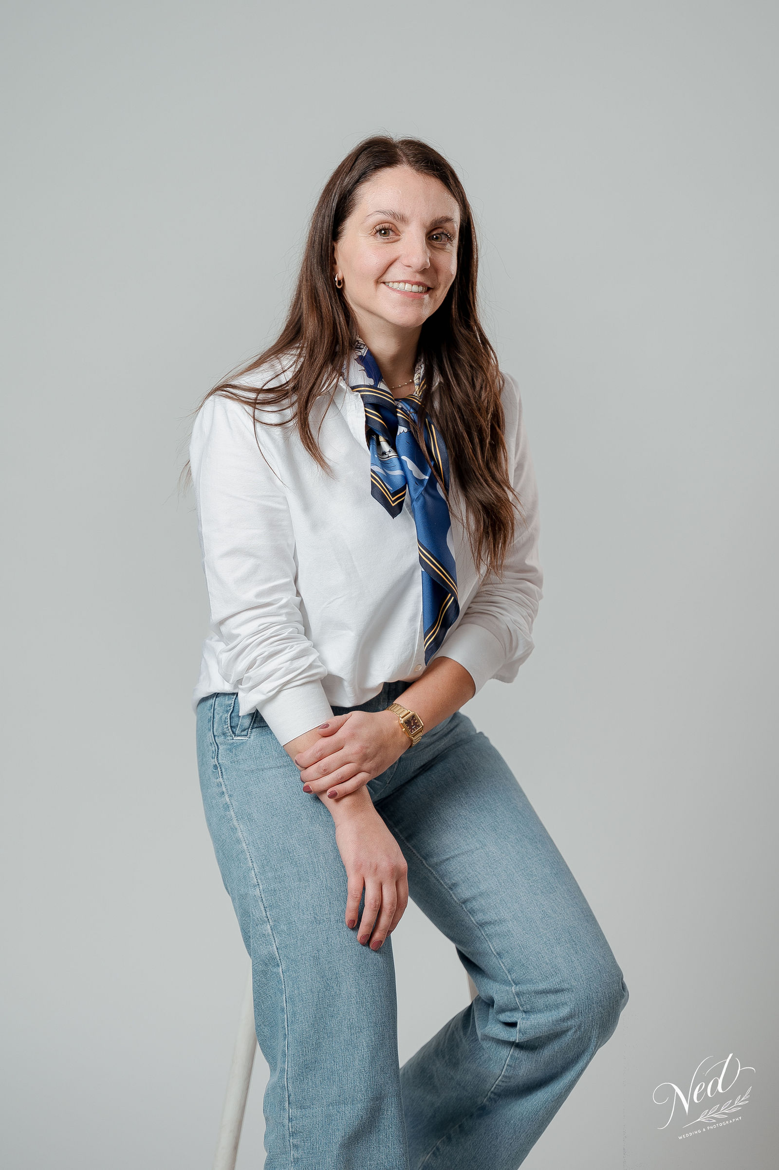 Femme souriante en blouse blanche et foulard bleu marine, jean clair, posant face à l'appareil en studio