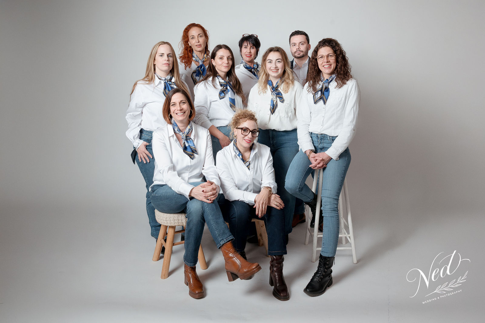 Neuf femmes en chemises blanches et foulards bleus posent ensemble en studio sur fond gris
