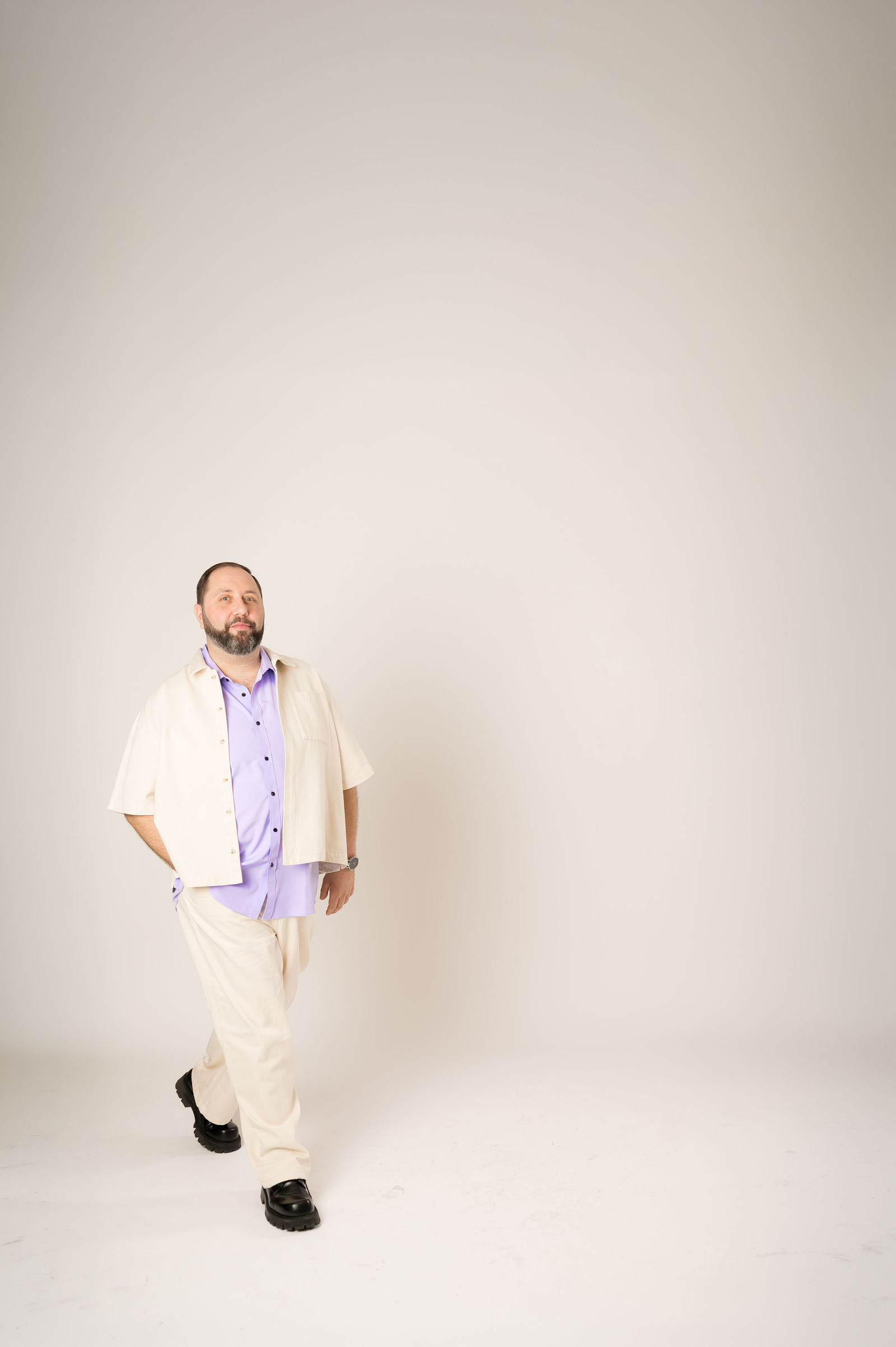 Homme en costume blanc et chemise violette posant en studio sur fond neutre