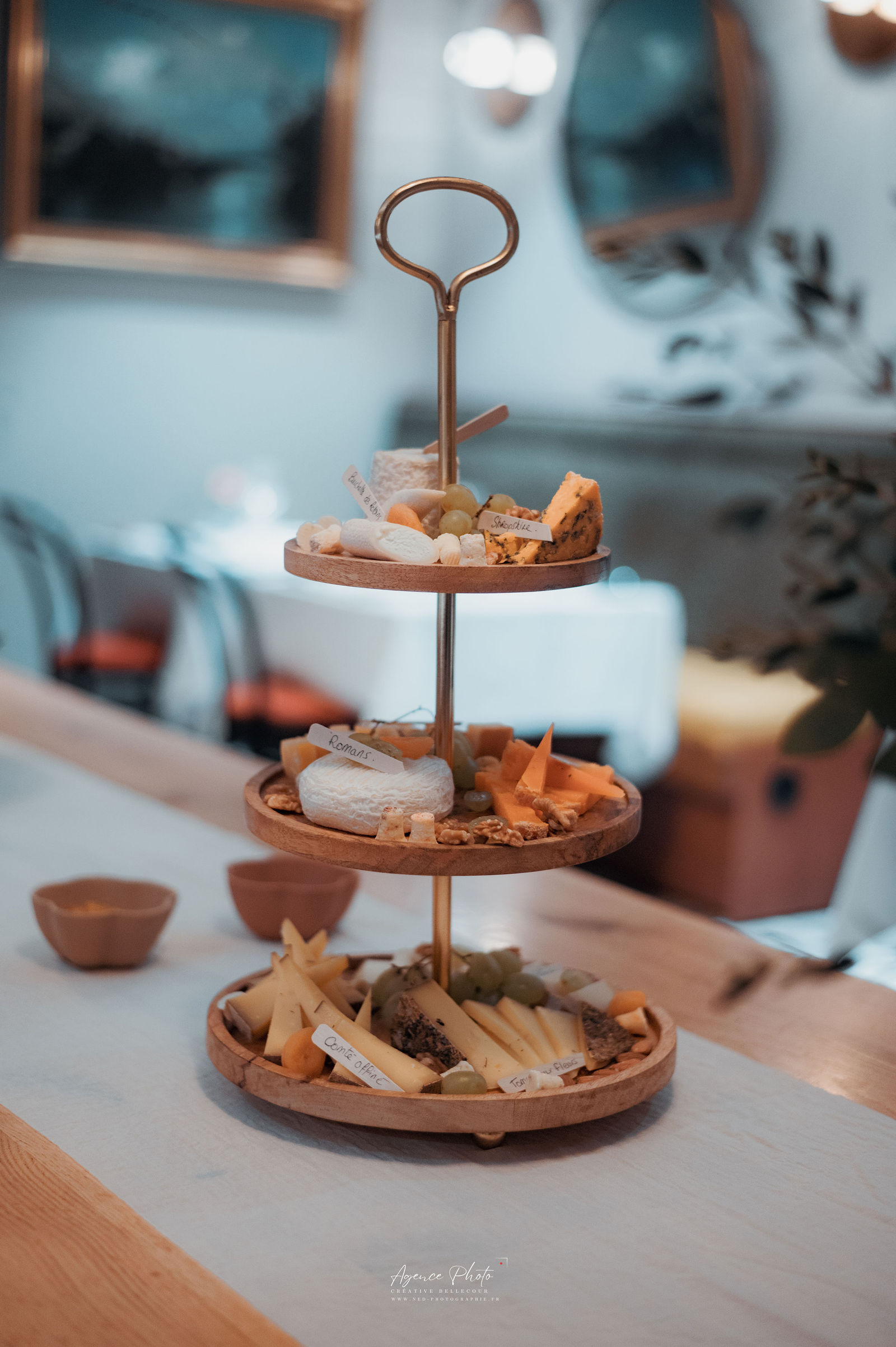 Présentoir trois étages en bois avec poignée doré contenant différents gâteaux et pâtisseries, sur table beige