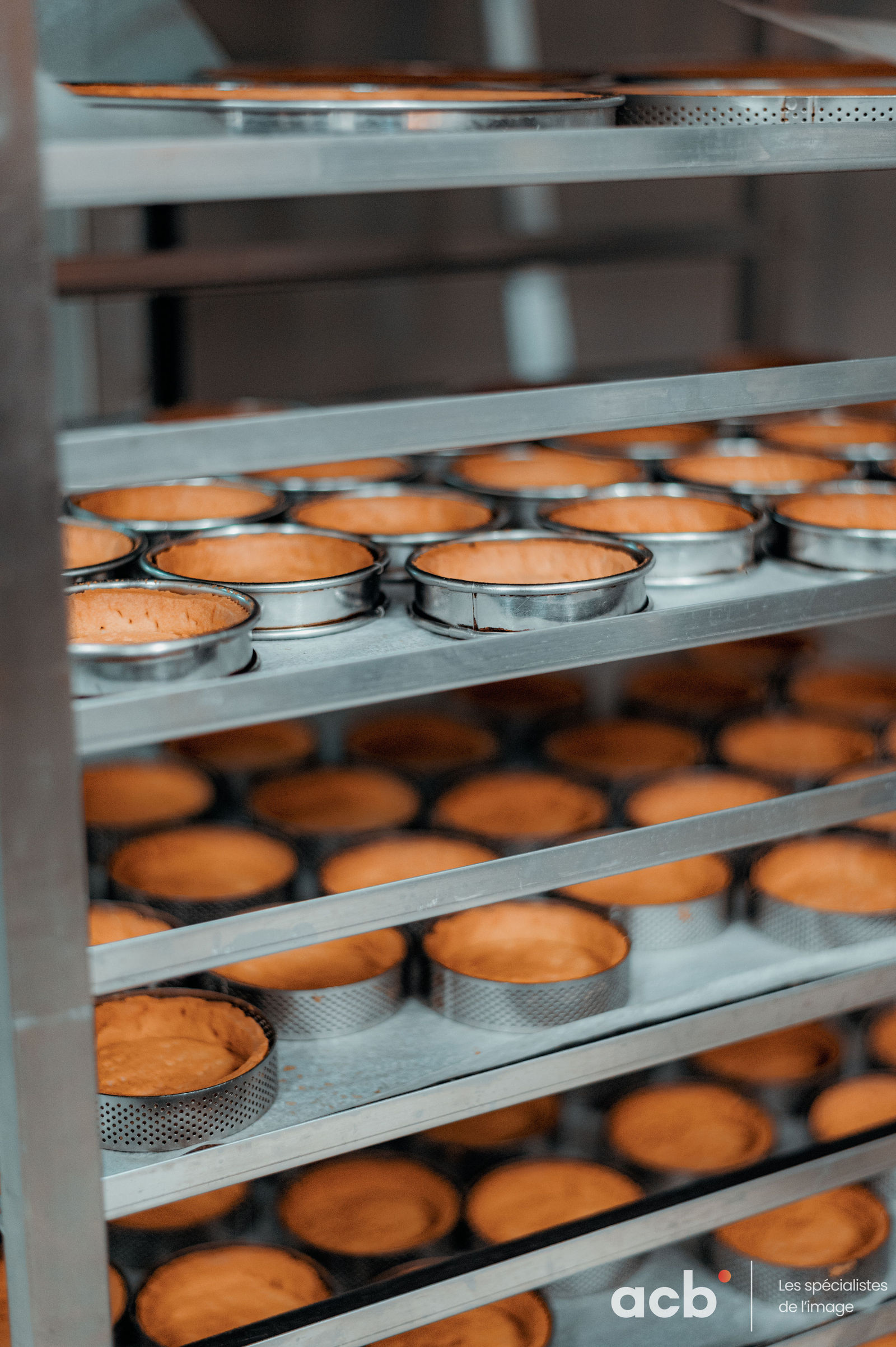 Plusieurs étages de moules métalliques remplis de gâteaux dorés en cours de cuisson dans un four professionnel