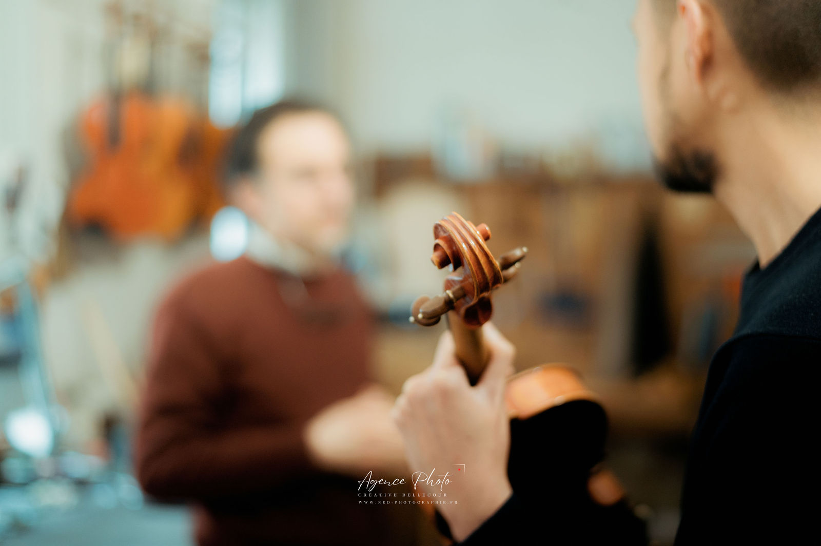 Musicien tenant un violon lors d'un atelier photo en intérieur, autres participants flous en arrière-plan