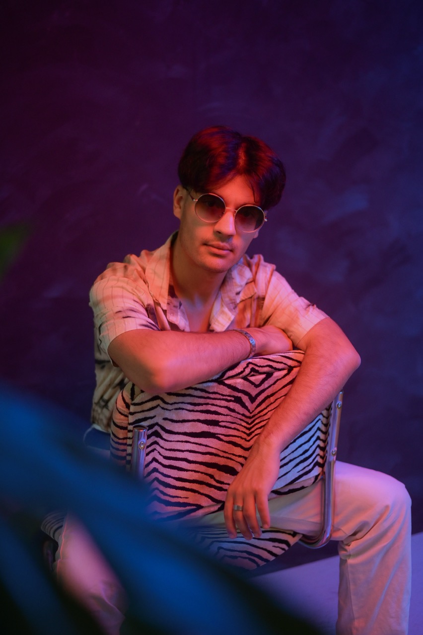 Homme assis portant lunettes rondes et chemise à motifs zébrés, éclairage néon rose et bleu