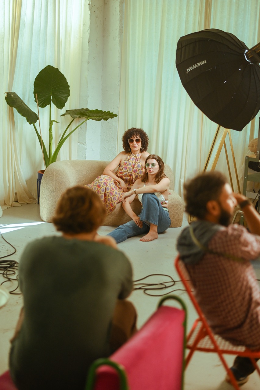 Deux femmes posent sur un fauteuil beige en studio photo, participants et formateur visible au premier plan