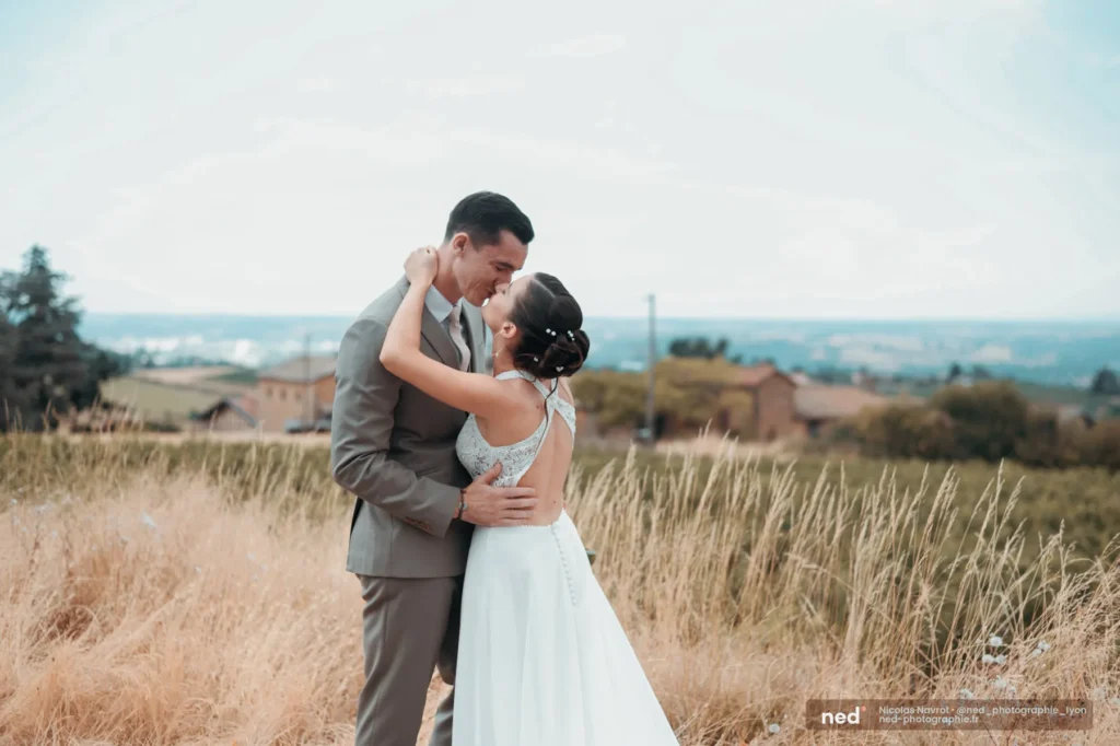 Les mariés s'embrassent dans les herbes hautes face aux vignes du Beaujolais, mariage au Domaine de Bellevue à Anse près de Villefranche-sur-Saône