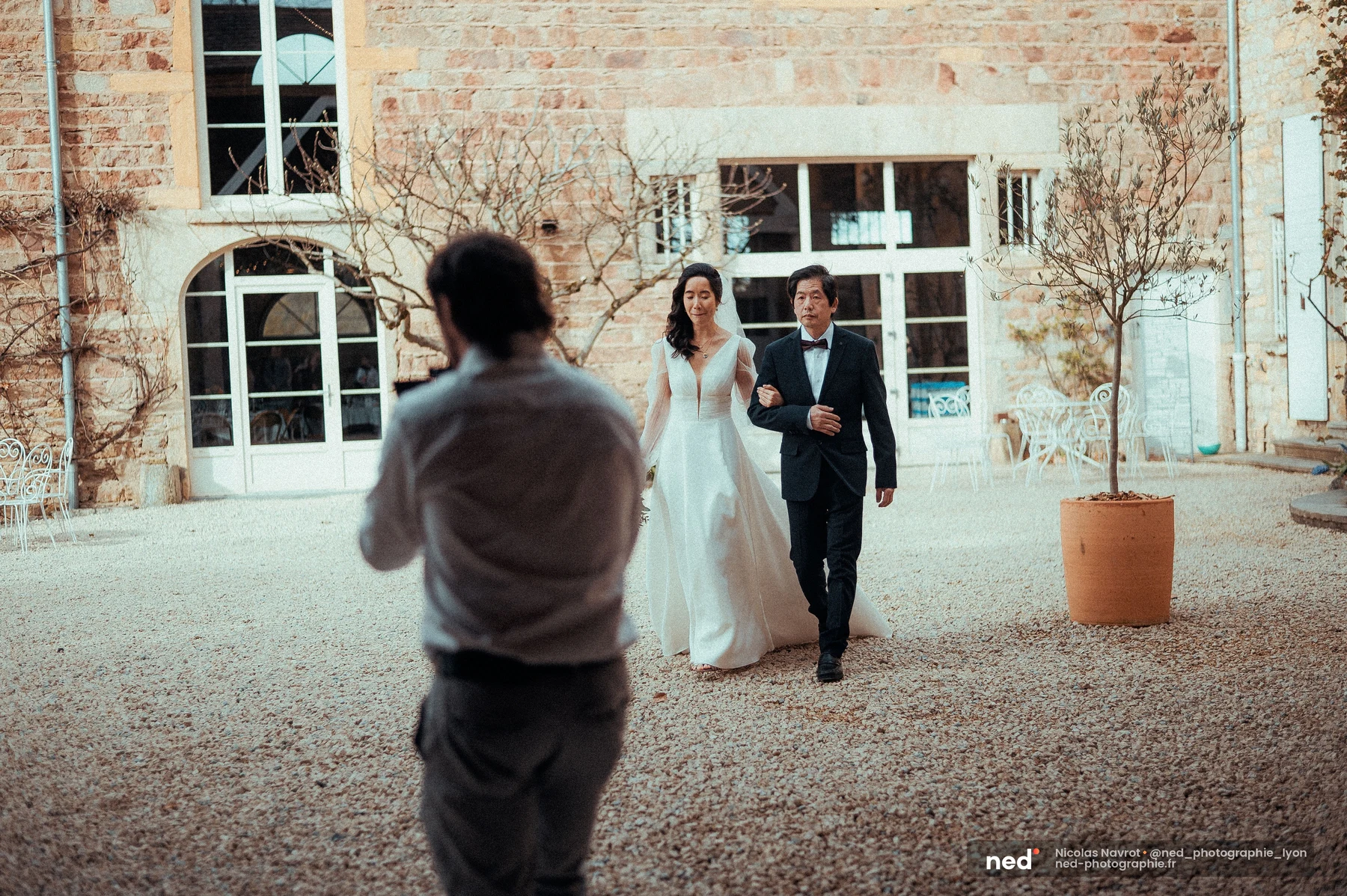 Mariée robe blanche coupe A voile long traversant cour domaine en pierre, mariage au Domaine de Tourieux