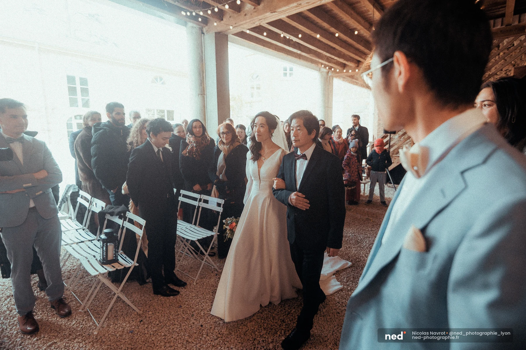 Mariée robe blanche voile remontant allée cérémonie charpente bois guirlandes, mariage au Domaine de Tourieux