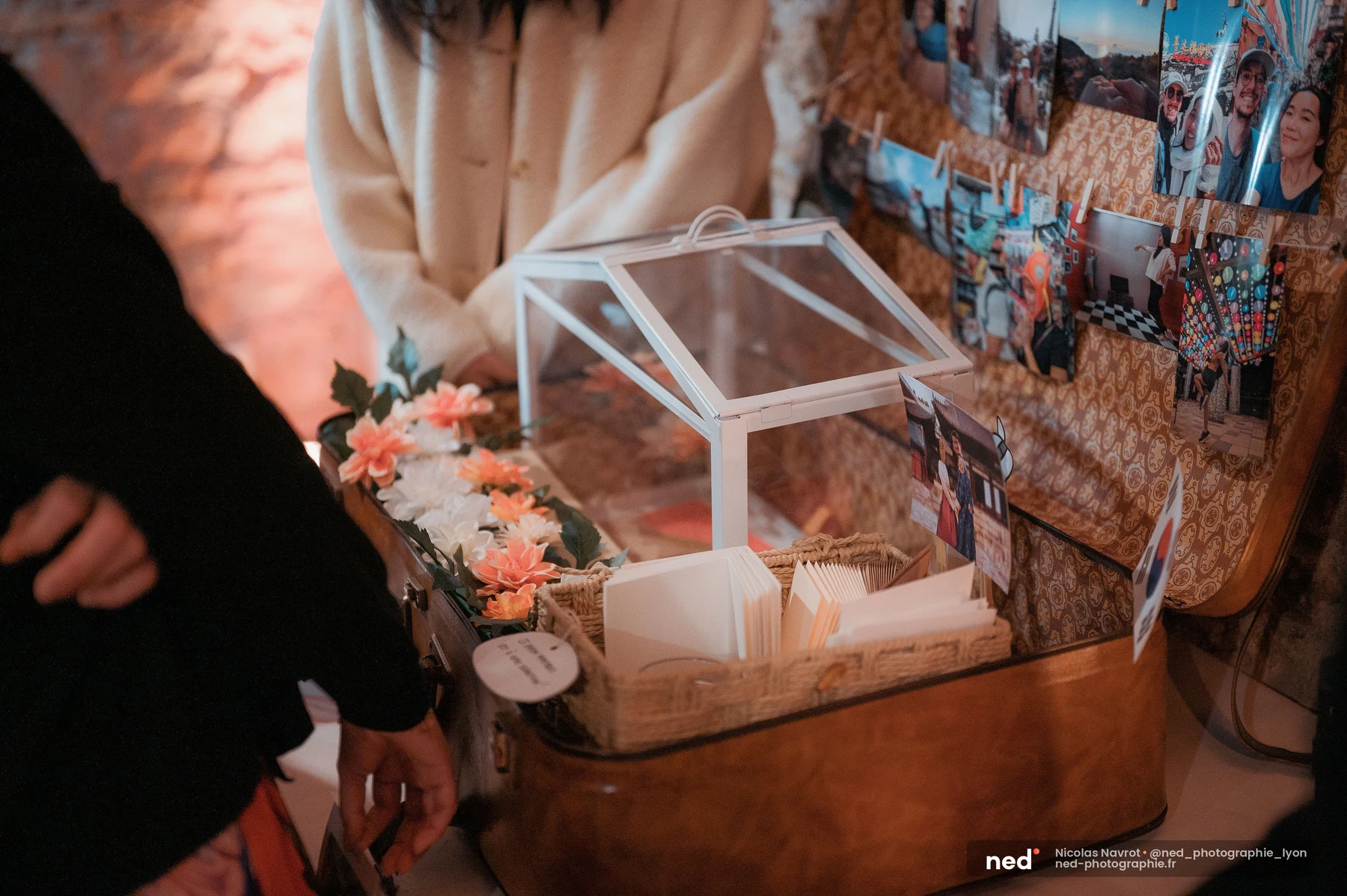 Urne mariage en verre sur valise vintage, fleurs corail et mur de photos, mariage au Domaine de Tourieux