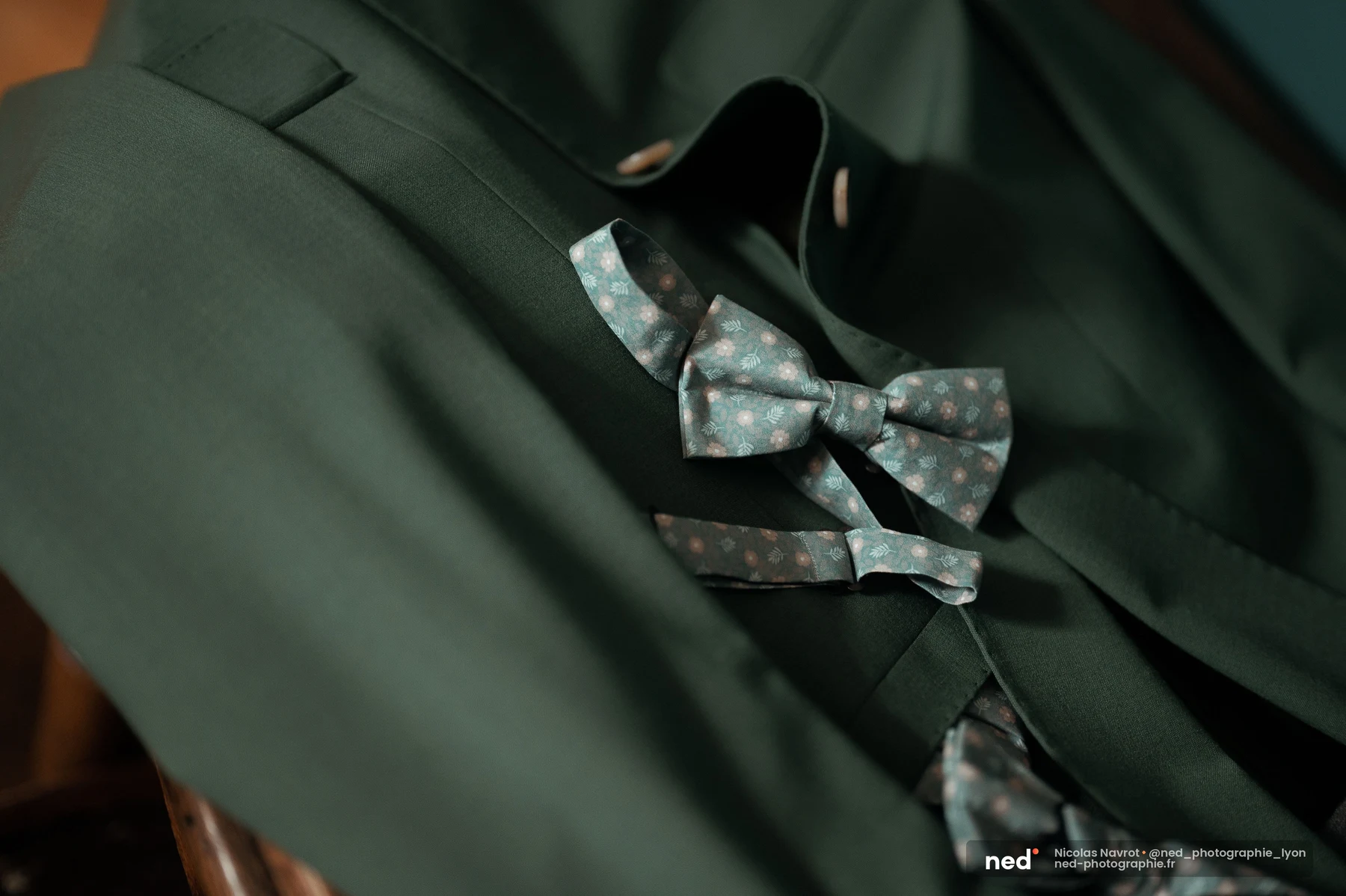 Nœud papillon floral bleu-gris posé sur costume vert sapin de marié, mariage au Domaine de Tourieux