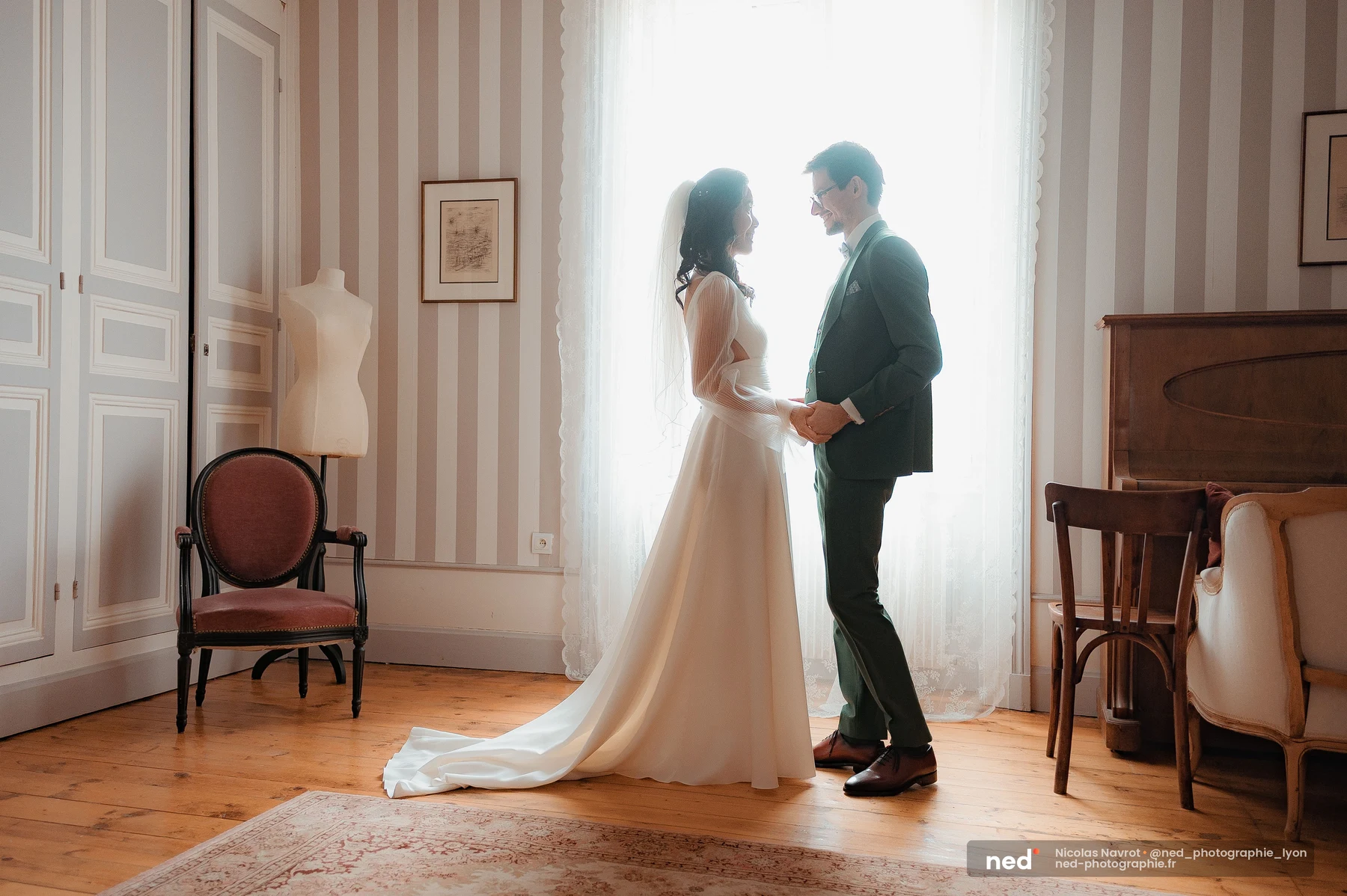 First look mariés robe blanche costume vert sapin contre-jour fenêtre château, mariage au Domaine de Tourieux