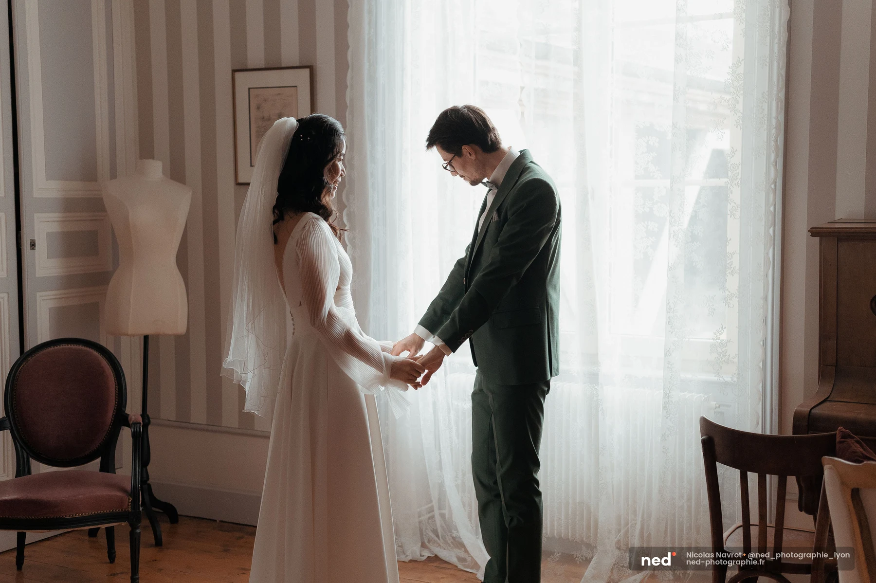 Mariés se tenant les mains first look fenêtre lumineuse costume vert robe blanche, mariage au Domaine de Tourieux