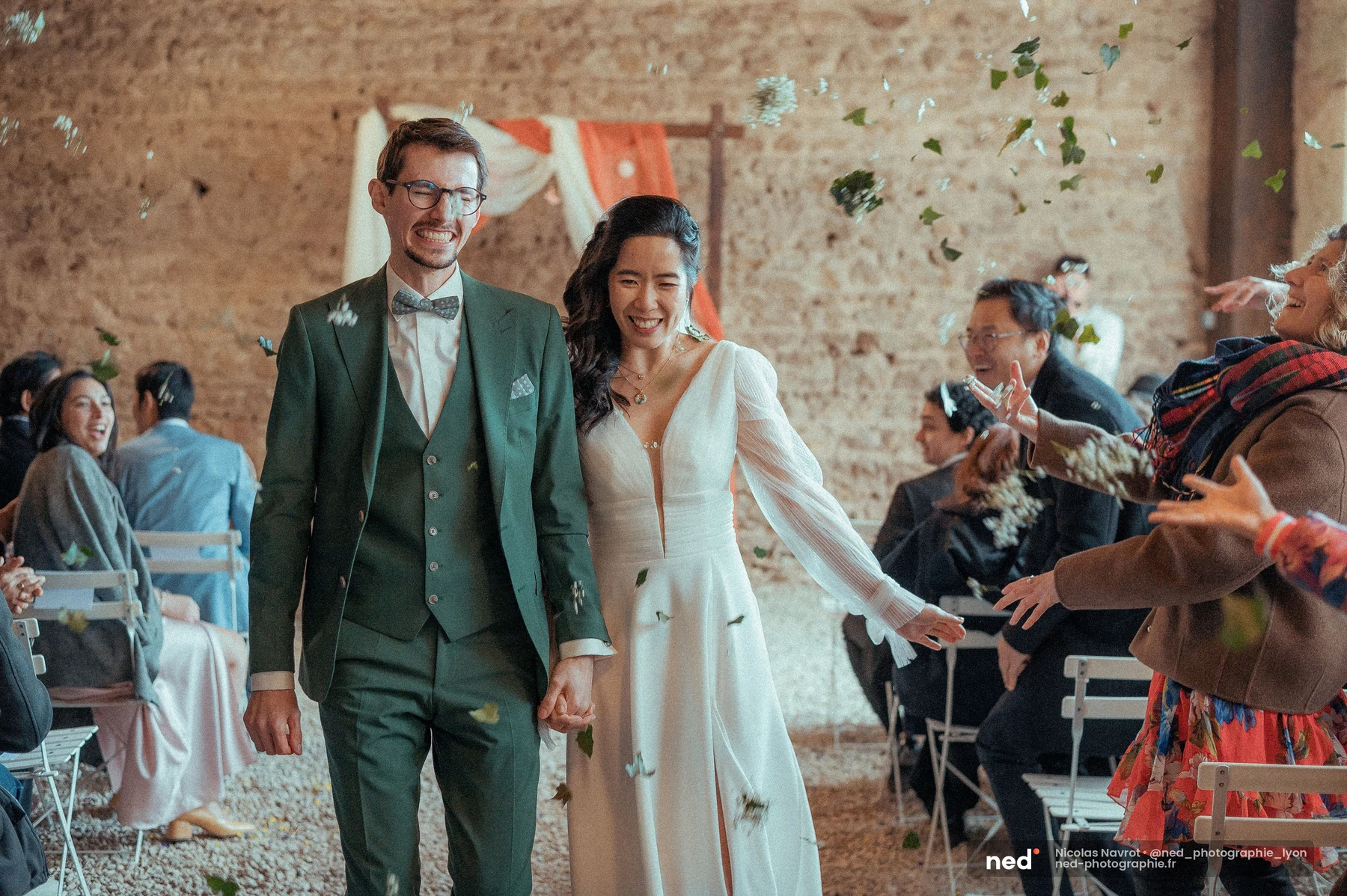 Mariés remontant l'allée en grange entourés de confettis de feuilles lancés par les invités, mariage au Domaine de Touri